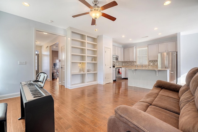 living room featuring built in shelves, ceiling fan, and light hardwood / wood-style floors