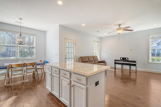 kitchen with dark wood-type flooring, a kitchen island, decorative light fixtures, white cabinets, and ceiling fan with notable chandelier