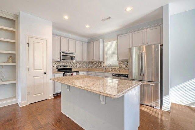 kitchen with a kitchen breakfast bar, light stone countertops, a kitchen island, dark hardwood / wood-style flooring, and stainless steel appliances