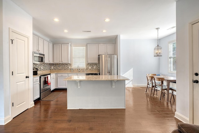 kitchen with a center island, dark wood-type flooring, light stone countertops, appliances with stainless steel finishes, and decorative light fixtures