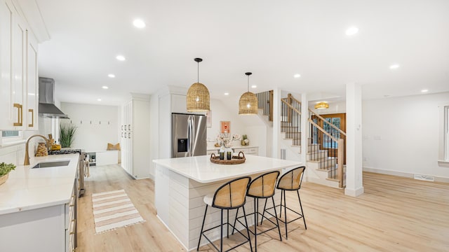 kitchen with wall chimney exhaust hood, hanging light fixtures, a center island, white cabinets, and appliances with stainless steel finishes