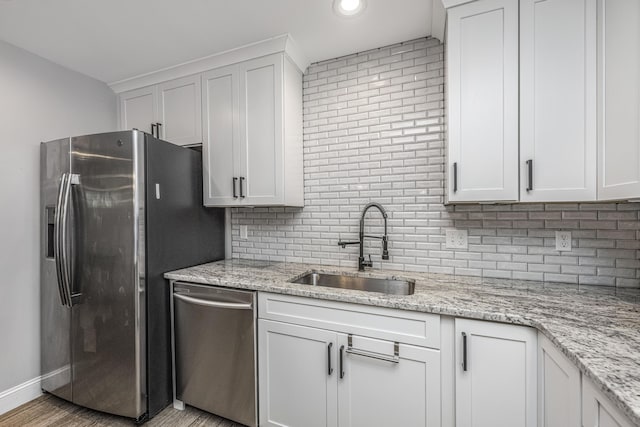 kitchen featuring light stone counters, backsplash, appliances with stainless steel finishes, white cabinetry, and a sink