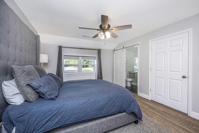 bedroom with a barn door, baseboards, visible vents, ensuite bath, and wood finished floors