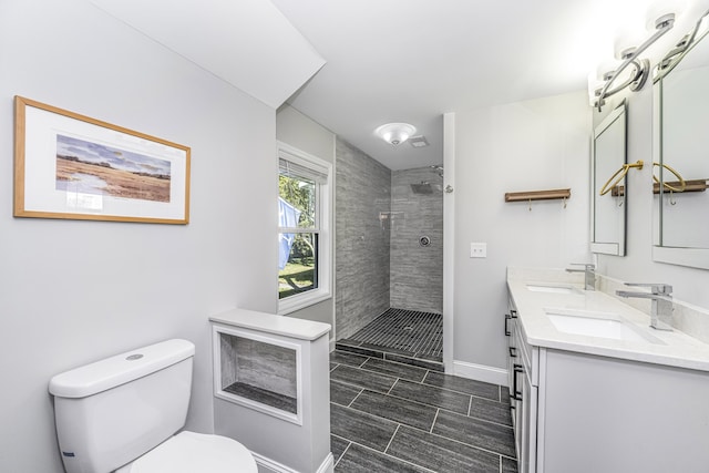 bathroom with baseboards, tiled shower, a sink, and toilet