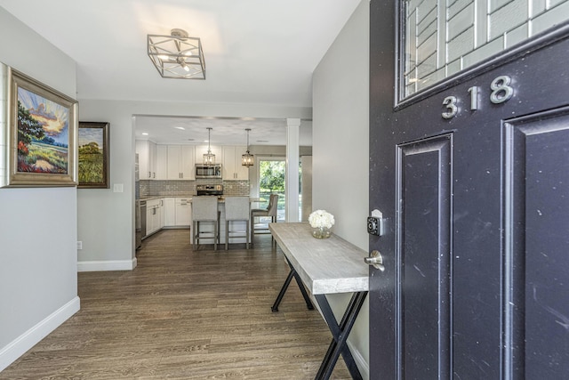 foyer with dark wood-type flooring, ornate columns, and baseboards