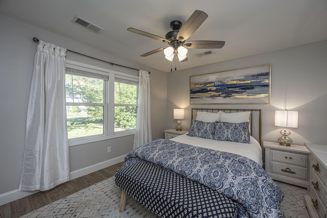 bedroom with a ceiling fan, visible vents, baseboards, and wood finished floors