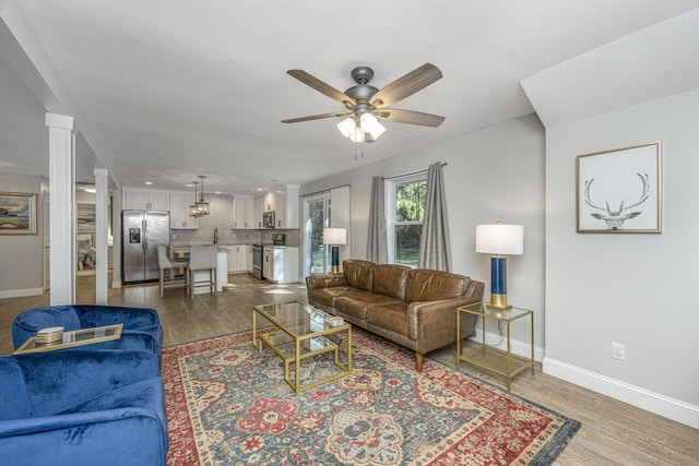 living area featuring baseboards, ceiling fan, ornate columns, and wood finished floors