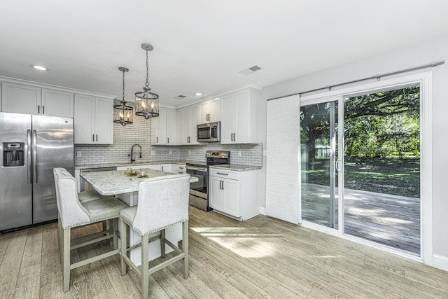 kitchen with stainless steel appliances, a sink, visible vents, light wood-style floors, and decorative backsplash