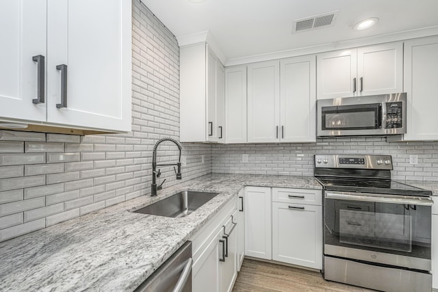 kitchen featuring stainless steel appliances, tasteful backsplash, visible vents, white cabinetry, and a sink