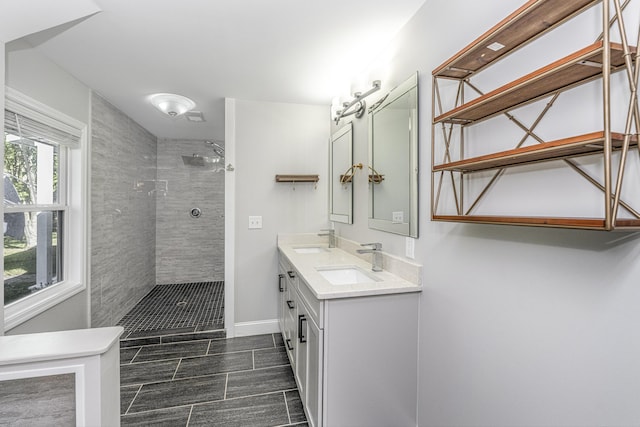 full bathroom featuring double vanity, baseboards, a tile shower, and a sink