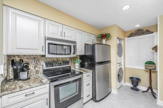 kitchen with white cabinetry, stainless steel appliances, stacked washing maching and dryer, and dark stone countertops