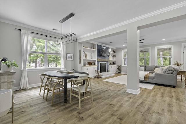 dining space featuring crown molding, baseboards, ceiling fan with notable chandelier, a glass covered fireplace, and light wood-style flooring