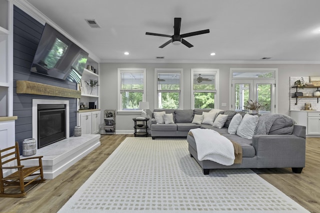 living room with crown molding, recessed lighting, a large fireplace, a ceiling fan, and light wood finished floors