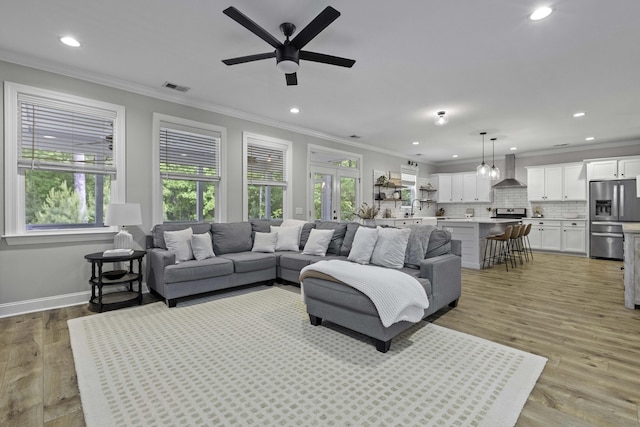 living area with visible vents, ornamental molding, recessed lighting, light wood-type flooring, and a ceiling fan
