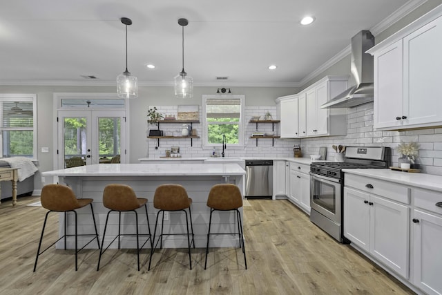kitchen with wall chimney range hood, open shelves, appliances with stainless steel finishes, a center island, and a kitchen bar