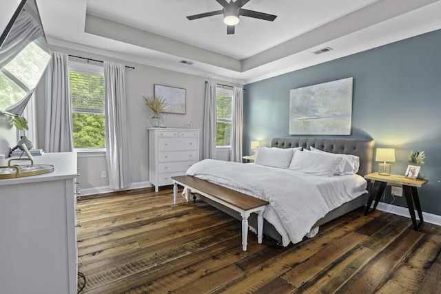 bedroom with a tray ceiling, visible vents, dark wood-style floors, and multiple windows