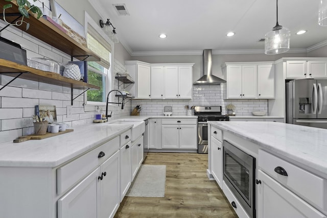 kitchen featuring wall chimney range hood, appliances with stainless steel finishes, a sink, decorative backsplash, and ornamental molding