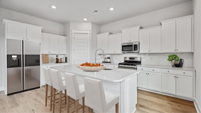 kitchen with decorative backsplash, an island with sink, appliances with stainless steel finishes, light wood-style floors, and white cabinetry