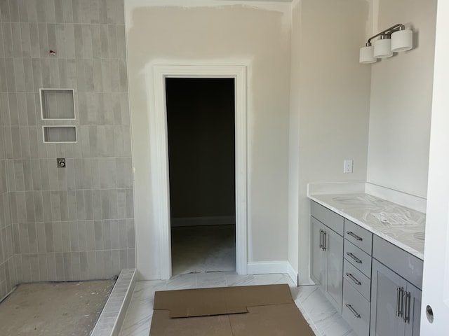 full bath with marble finish floor, tiled shower, vanity, and baseboards