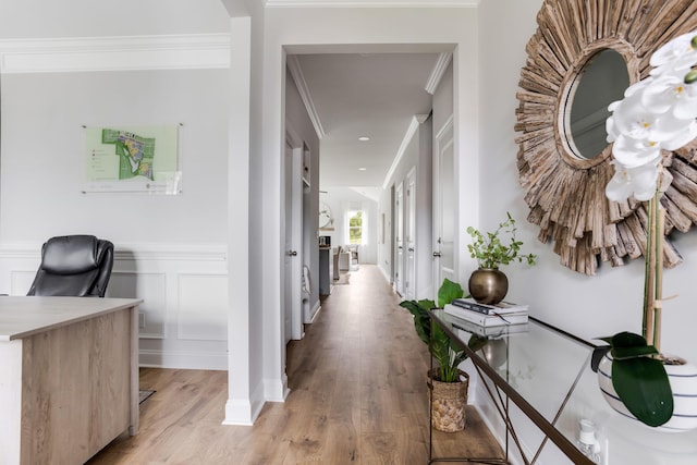 hall featuring light wood finished floors, a decorative wall, crown molding, and a wainscoted wall