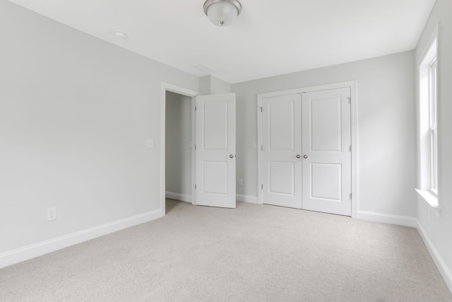 unfurnished bedroom featuring light carpet, a closet, and baseboards