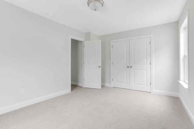 unfurnished bedroom featuring a closet, light carpet, baseboards, and multiple windows