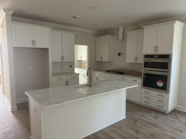 kitchen with a kitchen island with sink, a sink, visible vents, white cabinets, and ornamental molding