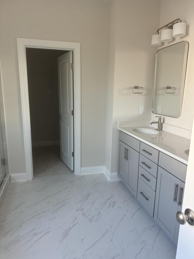 bathroom with double vanity, baseboards, marble finish floor, a shower stall, and a sink