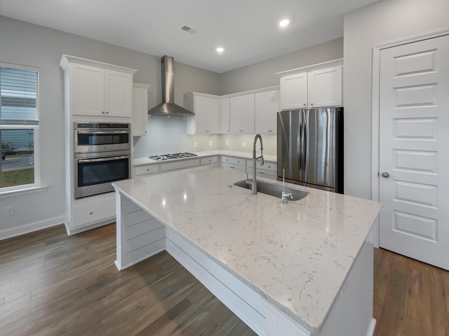 kitchen featuring a kitchen island with sink, sink, wall chimney exhaust hood, white cabinetry, and stainless steel appliances