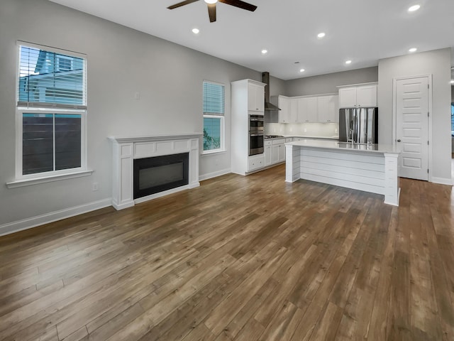 unfurnished living room featuring a wealth of natural light, ceiling fan, and dark wood-type flooring