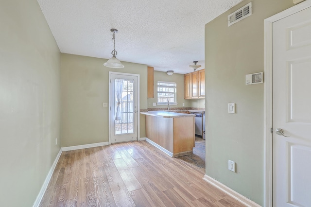 kitchen featuring pendant lighting, sink, dishwasher, light hardwood / wood-style floors, and a textured ceiling