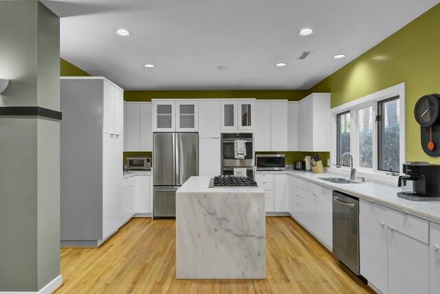 kitchen with appliances with stainless steel finishes, a kitchen island, a sink, and white cabinets