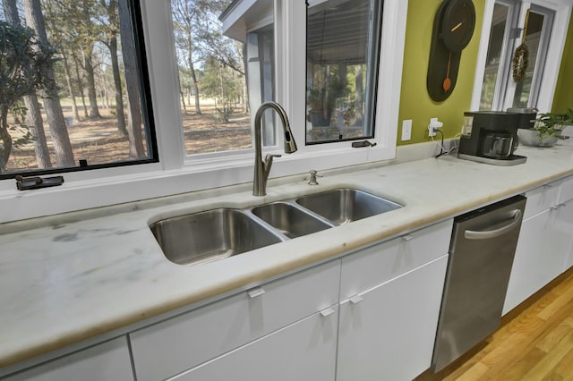 kitchen with light countertops, stainless steel dishwasher, white cabinetry, a sink, and light wood-type flooring