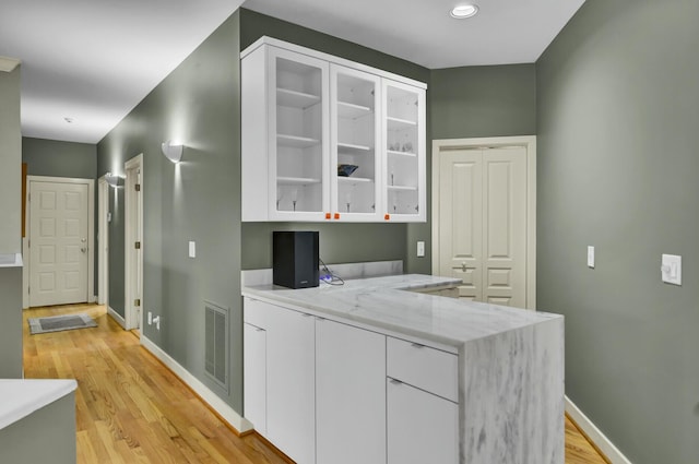 kitchen featuring baseboards, visible vents, white cabinets, glass insert cabinets, and light wood-style floors