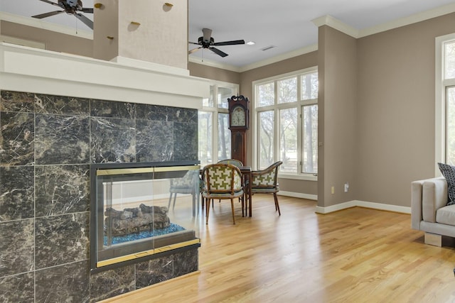 living area with a tile fireplace, wood finished floors, a ceiling fan, baseboards, and ornamental molding