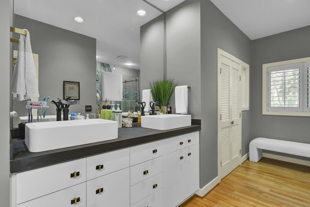 bathroom featuring double vanity, a shower stall, a sink, and wood finished floors