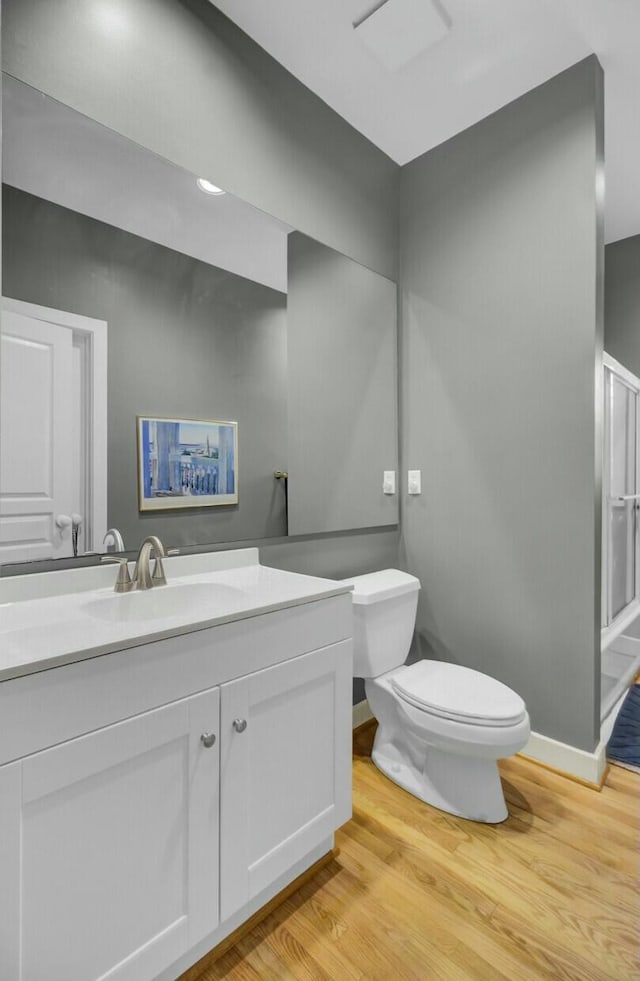 bathroom with toilet, wood finished floors, vanity, baseboards, and a shower