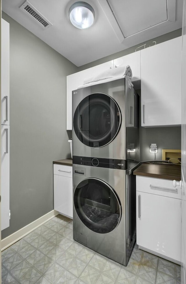 clothes washing area with visible vents, baseboards, stacked washing maching and dryer, cabinet space, and light floors