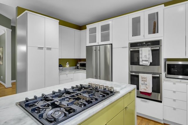 kitchen featuring light stone counters, a toaster, appliances with stainless steel finishes, glass insert cabinets, and white cabinets