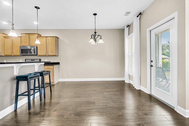 kitchen featuring hanging light fixtures, a breakfast bar, light brown cabinetry, an inviting chandelier, and dark hardwood / wood-style flooring