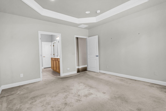 unfurnished bedroom with ensuite bath, a raised ceiling, and light colored carpet