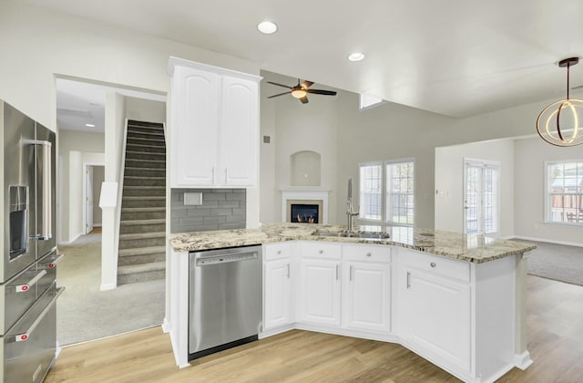 kitchen with stainless steel appliances, a sink, white cabinets, open floor plan, and decorative light fixtures