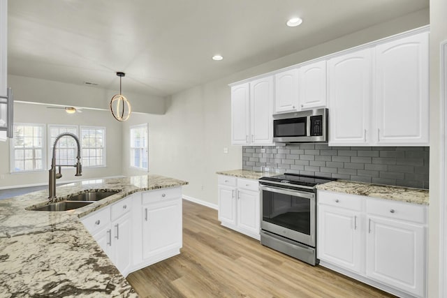 kitchen with hanging light fixtures, appliances with stainless steel finishes, a sink, and white cabinetry