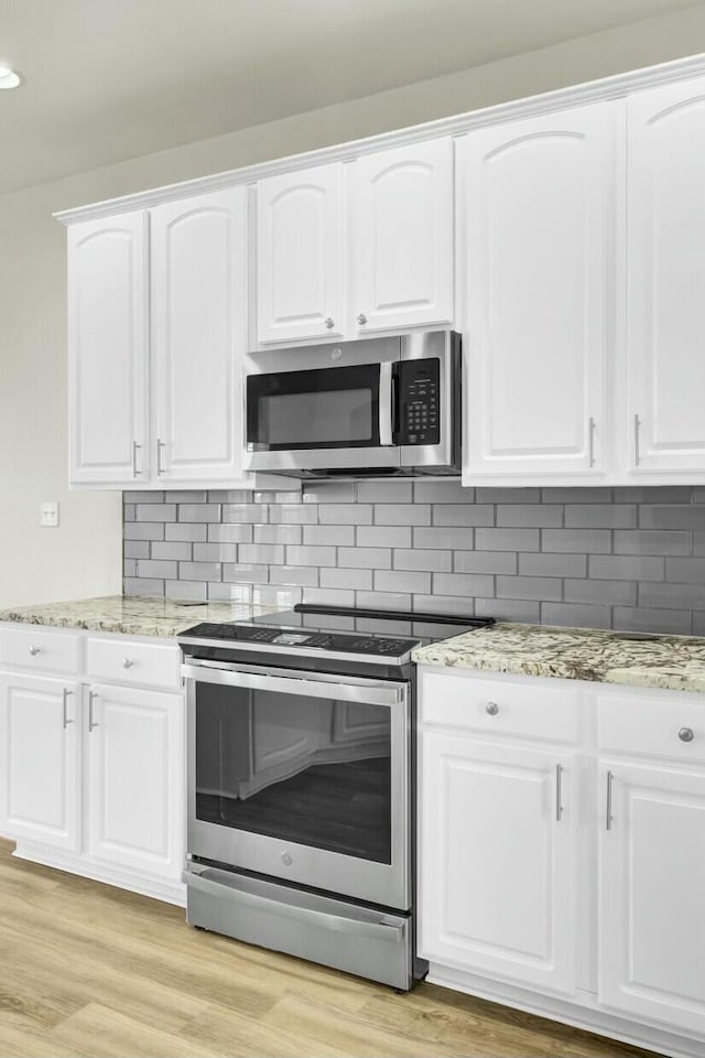 kitchen featuring white cabinets, light wood-type flooring, tasteful backsplash, and stainless steel appliances