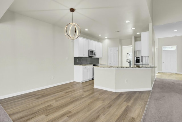 kitchen with light stone counters, light wood-style flooring, white cabinets, appliances with stainless steel finishes, and tasteful backsplash