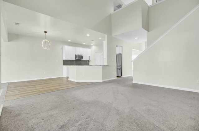 unfurnished living room featuring baseboards, recessed lighting, a towering ceiling, and light colored carpet