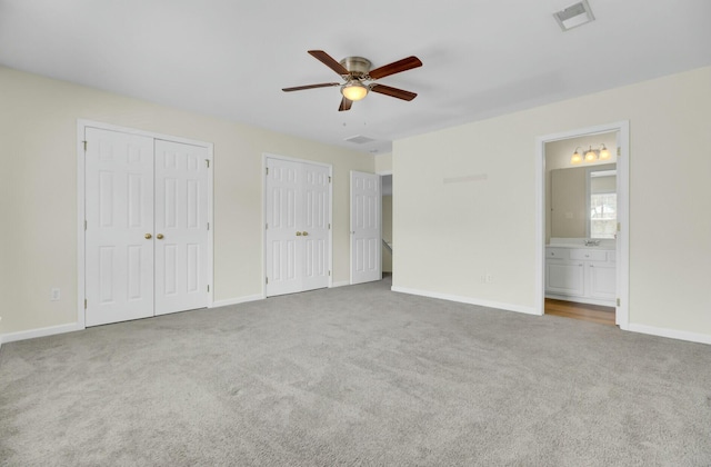 unfurnished bedroom with multiple closets, visible vents, light carpet, and baseboards