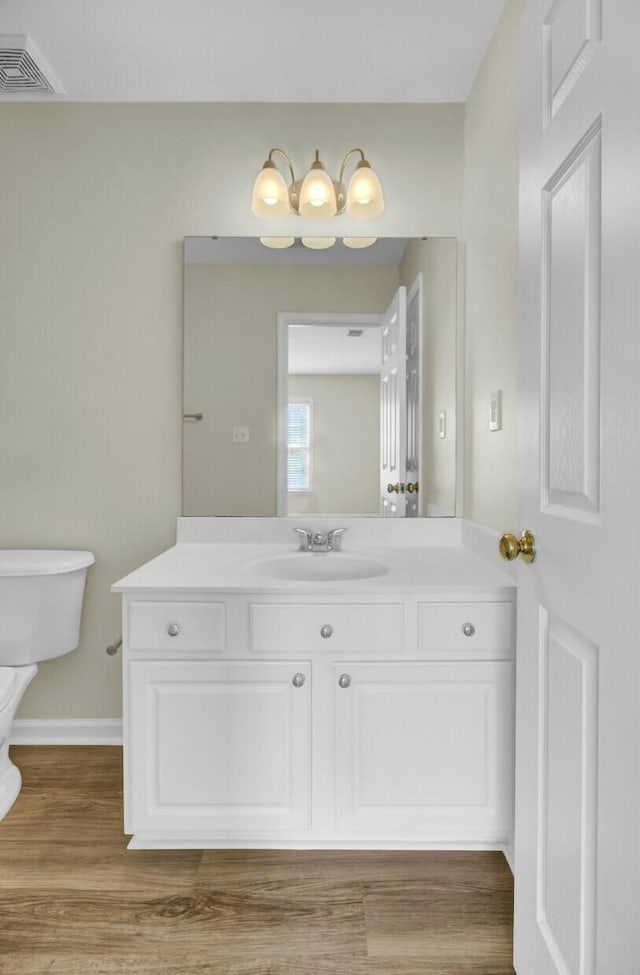 bathroom with toilet, wood finished floors, vanity, visible vents, and baseboards