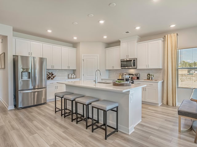 kitchen with sink, stainless steel appliances, a kitchen island with sink, white cabinets, and light wood-type flooring