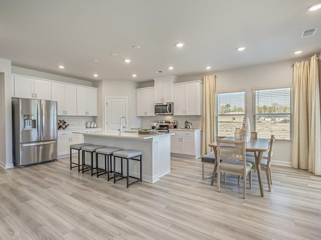 kitchen featuring appliances with stainless steel finishes, light hardwood / wood-style floors, white cabinetry, and an island with sink